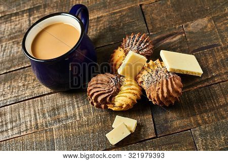 Scattered Double Color Cookies Near Pieces Of White Porous Chocolate And Full Cup Of Coffee With Mil