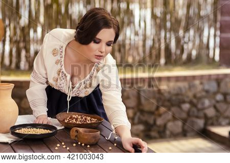 Portrait Of Sexy Brunette Girl In Village Dress Picking Colorful Kidney Beans On Table In Village En