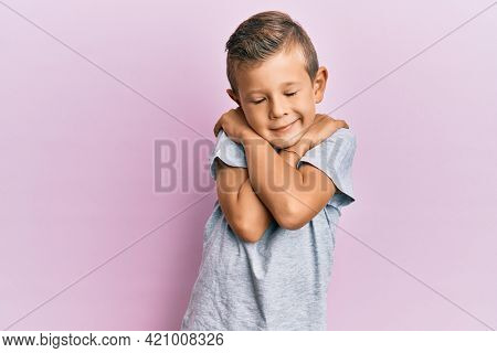 Adorable caucasian kid wearing casual clothes hugging oneself happy and positive, smiling confident. self love and self care 