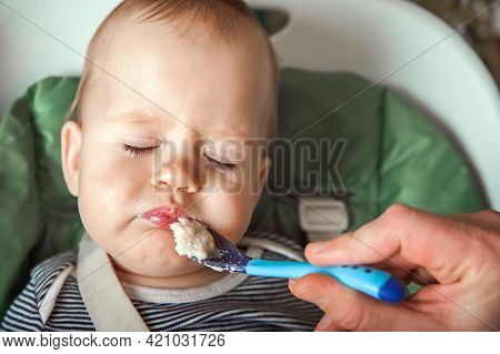 Funny Portrait Of Toddler Eating Close-up. Complementary Feeding Of Child With Porridge At 9 Months.