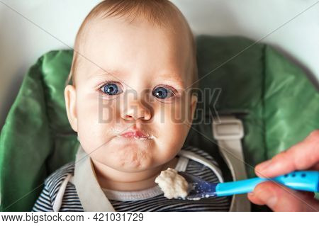 Funny Portrait Of Toddler Eating Close-up. Complementary Feeding Of Child With Porridge At 9 Months.