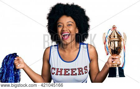 Young african american woman wearing cheerleader uniform holding pompom and trophy smiling and laughing hard out loud because funny crazy joke. 