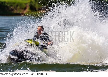 Krasnodar, Russia - July 25, 2020: Young Caucaisian Woman Drives Jet Ski Splashing At Sunset By Rive