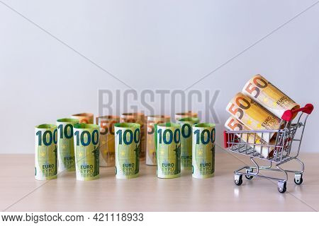 Euro Money In Denominations Of 100 And 50, Folded Into A Roll Of One Bill Each, And A Shopping Baske