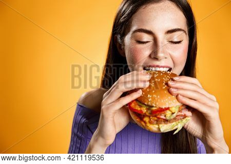 Girl Bites Cheeseburger With Satisfaction. Woman Eating Delicious Hambuger With Pleasure And Smile, 