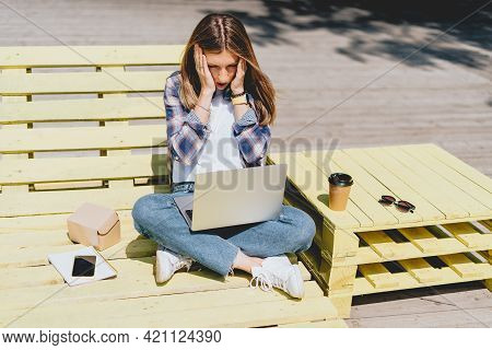 Beautiful Sad Thinking Woman Working At Laptop Outside And Drinking Coffee. Using Computer And Onlin