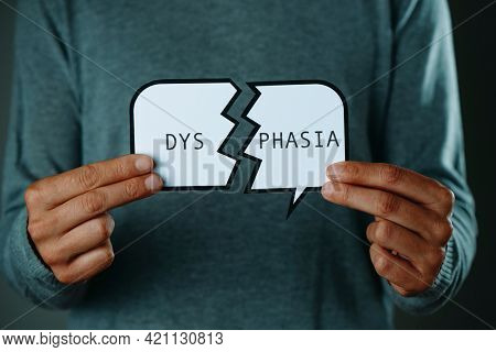 closeup of a young caucasian man holding a broken speech balloon, with the text dysphasia written in it, in front of him
