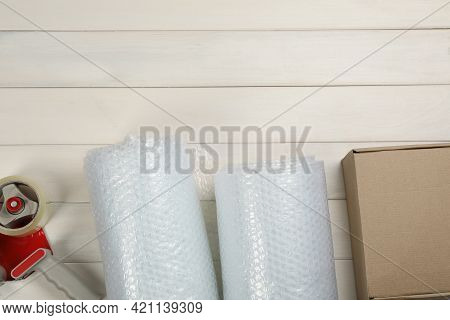 Bubble Wrap Rolls, Cardboard Box And Tape Dispenser On White Wooden Background, Flat Lay. Space For 