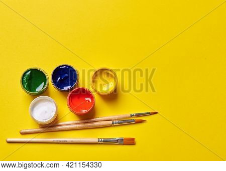 Several Brushes And Bright Paints On A Yellow Background