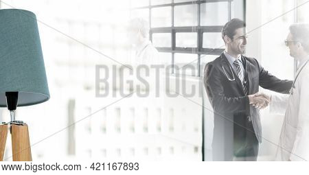 Composition of two smiling male doctors shaking hands in corridor with double exposure. healthcare, partnership and success concept digitally generated image.