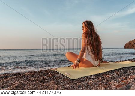 Young Woman With Long Hair In White Swimsuit And Boho Style Braclets Practicing Outdoors On Yoga Mat