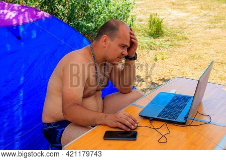 Man Using His Laptop Sitting At A Folding Picnic Table In A Camping. Working While Traveling. Freela