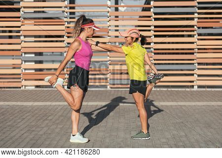 Two Multi-ethnic Girls Stretching Together In The Street, Stretching Their Legs Before A Run. Lesbia