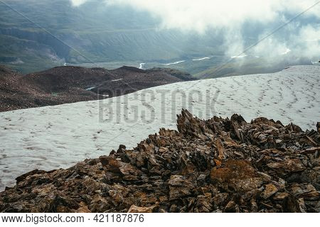 View From Precipice Edge With Sharp Rocks And Snow Cornice To Mountain Valley In Low Clouds. Wonderf