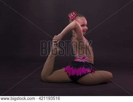 Happy Smiling Ittle Girl In Gymnast In Costume Sitting In Position In Studio, Trying To Do Circle Wi
