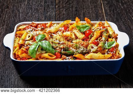 Ground Turkey Penne Pasta Bake With Asparagus, Tomatoes And Olives In A Baking Dish On A Dark Wooden