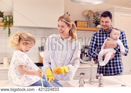 Smiling Family Having Fun In Kitchen Doing Washing Up At Sink Together