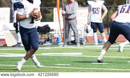 A High School Football Quarterback Is Dropping Back During A During A Passing Play Crossing His Legs
