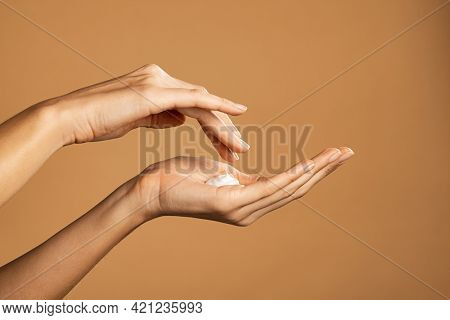 Close up shot of beautiful female hands holding and applying moisturiser. Beauty woman hand applying cream. Beautiful girl on creamy background holding moisturizer.