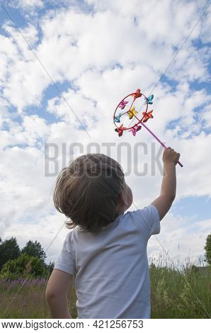 Small Kid Holding Colorful Bright Rainbow Toy Pinwheel Against Blue Sky With Clouds