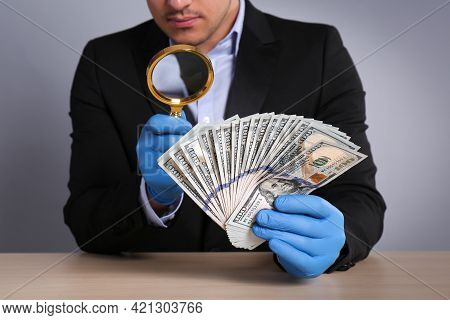 Expert Authenticating 100 Dollar Banknotes With Magnifying Glass At Table On Light Grey Background, 