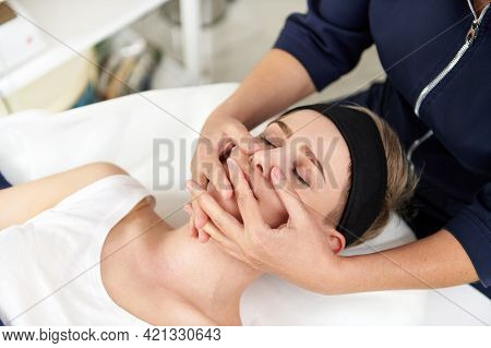 Close Up Portrait Of Aesthetician Hands Doing Professional Rejuvenating Face Massage To Young Blonde