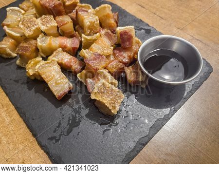 Close Up Of A Plate Of Fried Torreznos Or Fried Rashers On A Black Slate Plate And A Jar With Barbec