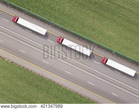 Dump Trucks Carrying Goods On The Highway. Red Truck Driving On Asphalt Road Along The Green Fields.