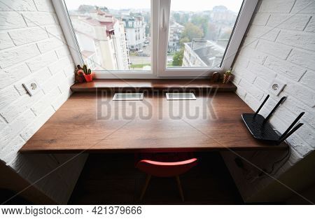 Close Up Of Wooden Desk Built Into Recess Of White Wall In Front Of Window. Nearby Red Chair, Intern