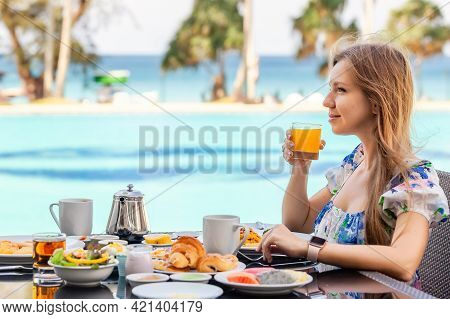 Smiling Woman On American Breakfast Drinking Orange Juice Next To Poolside In Resort. Morning Food N