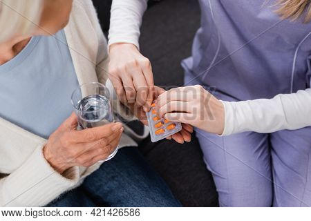 Partial View Of Nurse Giving Medication To Aged Woman Holding Glass Of Water.