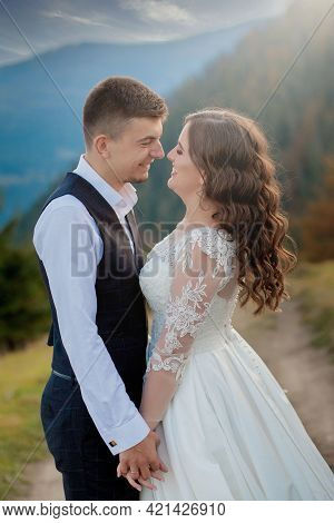 Beautiful Couple On Their Wedding Day Against The Background Of An Epithetical Sunset In The Mountai