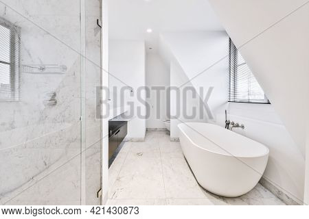 Interior Of Spacious Bathroom In Marble Tiles With Soaker Tub Near Window In Attic