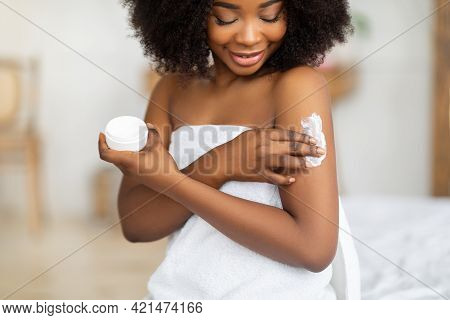 Beautiful Black Lady Wearing Towel After Bath, Applying Cream, Rubbing In Nourishing Body Butter At 