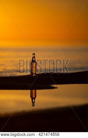 An Ice Cold Beer / Soda Bottle Standing Straight On The Golden Sands At Sunset. Summer Evening
