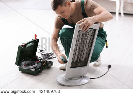 Professional Technician Repairing Electric Ultrared Heater With Screw Gun Indoors