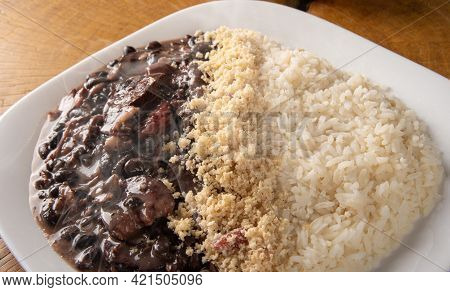 Brazilian Feijoada, White Dish With A Delicious Brazilian Feijoada, Rice And Farofa, With Two Orange