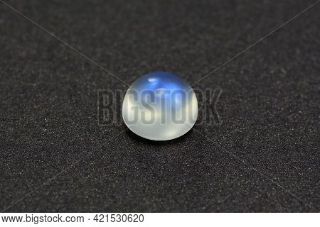 Natural Adularia Blue Sheen Round Cabochon Moonstone. Loose Gem On Gray Textured Leather Background.