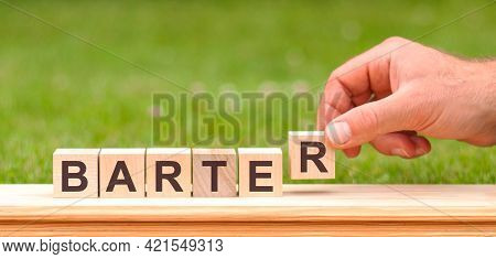Barter Is A Word Written On Wooden Blocks. A Man's Hand Holds A Wooden Cube With The Letter R From T