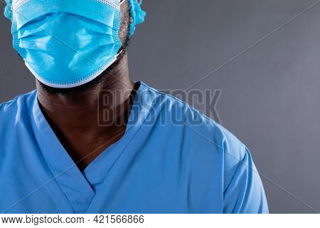 Mid section of african american male health worker wearing face mask against grey background. healthcare and medical professionalism concept