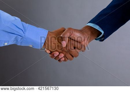 Mid section of two businessmen shaking hands against grey background. business agreement and professionalism concept