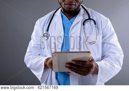 Mid section of african american male doctor using digital tablet against grey background. healthcare and medical professionalism concept