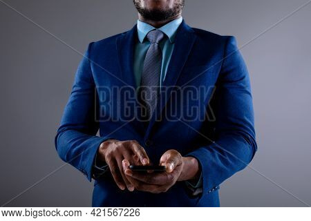 Mid section of african american businessman using smartphone against grey background. business, professionalism and technology concept