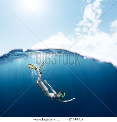Ung dam snorkling och dykning på ett andetag håll i ett klart tropiska hav med blå himmel med sol och