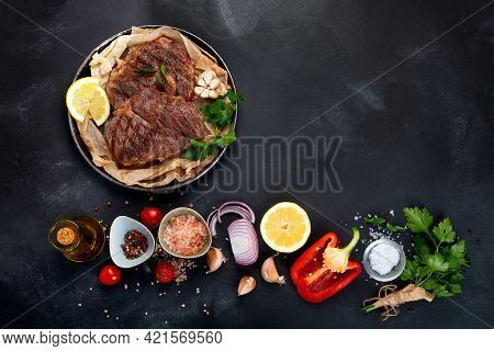 Delicious Prepared Meat Steaks With Seasoning And Herbs On Dark Background.