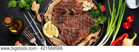 Delicious Prepared Meat Steaks With Seasoning And Herbs On Dark Background.