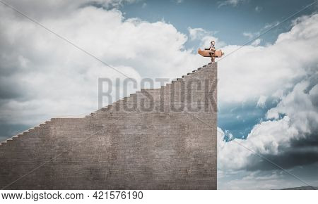 child dressed as an aviator with cardboard plane at the top of very high stairs. concept of freedom, lightheartedness, dreams.