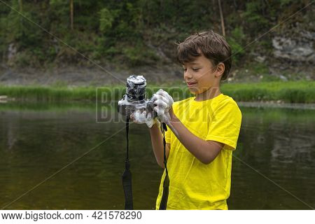 Naughty Kid Standing On Bank Of Mountain River Holding Digital Camera He Had Just Washed With Soap. 