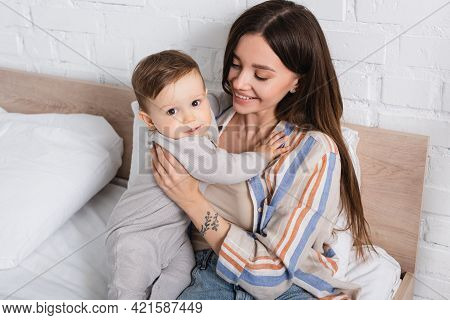 Happy Tattooed Mother Hugging Baby Boy In Romper.