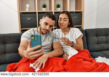 Young latin ill couple having medical teleconsultation using smartphone at home.